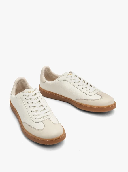 Cremige, sportliche Halbschuhe auf einem flachen, beigen Untergrund