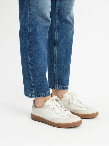 Cremige, sportliche Halbschuhe auf einem flachen, beigen Untergrund